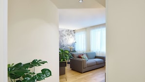 Un salon moderne avec un canapé gris, une grande plante verte et un mur décoratif.