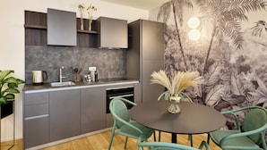 Une cuisine moderne avec des meubles gris, un plan de travail noir et un coin repas comprenant une table ronde et des chaises vertes.