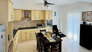 Una cocina moderna con armarios de madera clara, una mesa de comedor con sillas, un ventilador de techo y un mueble negro.