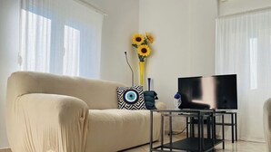 Una sala de estar con un sofá, un televisor sobre un mueble bajo y un jarrón con girasoles.