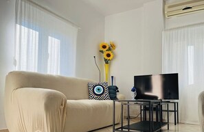 A living room with a sofa, a TV on a stand, and a vase with sunflowers. - LP Almyrida - 7 minutes walk from the beach (Almyrida)