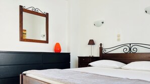 Quarto com cama de madeira, mesa de cabeceira, abajur, espelho e um vaso vermelho em um aparador.