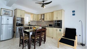 Cozinha compacta com armários de madeira, uma mesa de jantar com cadeiras, um ventilador de teto e uma cadeira preta.