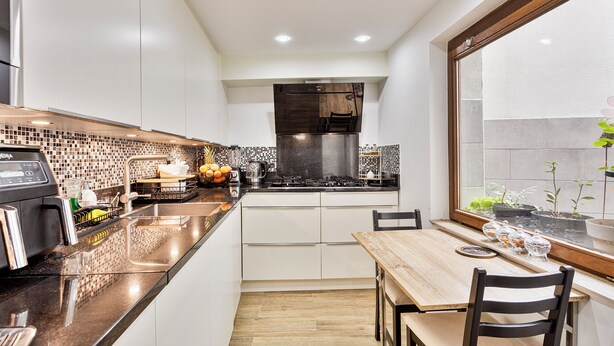 A modern kitchen with white cabinets, a black countertop, and a wooden dining table with chairs. - Beautiful room (Molenbeek-Saint-Jean)