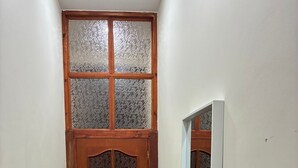 A narrow hallway with a wooden door featuring frosted glass panels, a potted plant, and a mirror on the wall. - Beautiful room (Molenbeek-Saint-Jean)