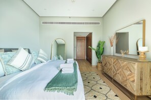 A bedroom with a bed, bedside tables, a mirror, a dresser, and a door leading to another room. - Bloomfields 2BR-Marquis 2020-Arjan (Dubai)