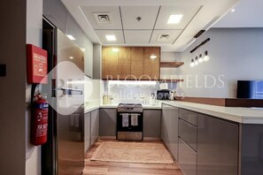 A modern kitchen with a built-in stove, stainless steel cabinets, and a wooden accent wall. - Bloomfields Marquis 2020 2br (Dubai)
