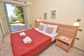 A hotel room with a bed, two bedside tables, a sliding glass door to an outdoor area, and two framed botanical prints on the wall. - Daphne Two Bedroom Apartment (Corfu)