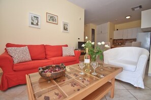A living room with a red sofa, a white sofa, a glass coffee table with a flower vase and wine glasses, and a small decorative bowl. - Daphne Two Bedroom Apartment (Corfu)