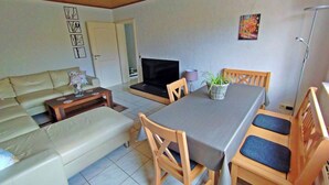 Un soggiorno con un divano, un tavolo da pranzo con sedie, una TV e una pianta.