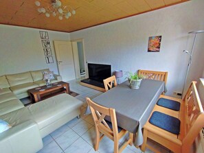 A living room with a sofa, a dining table with chairs, a TV, and a plant. - Cosy holiday flat in a quiet location, close to Luxembourg and Trier (Ralingen)