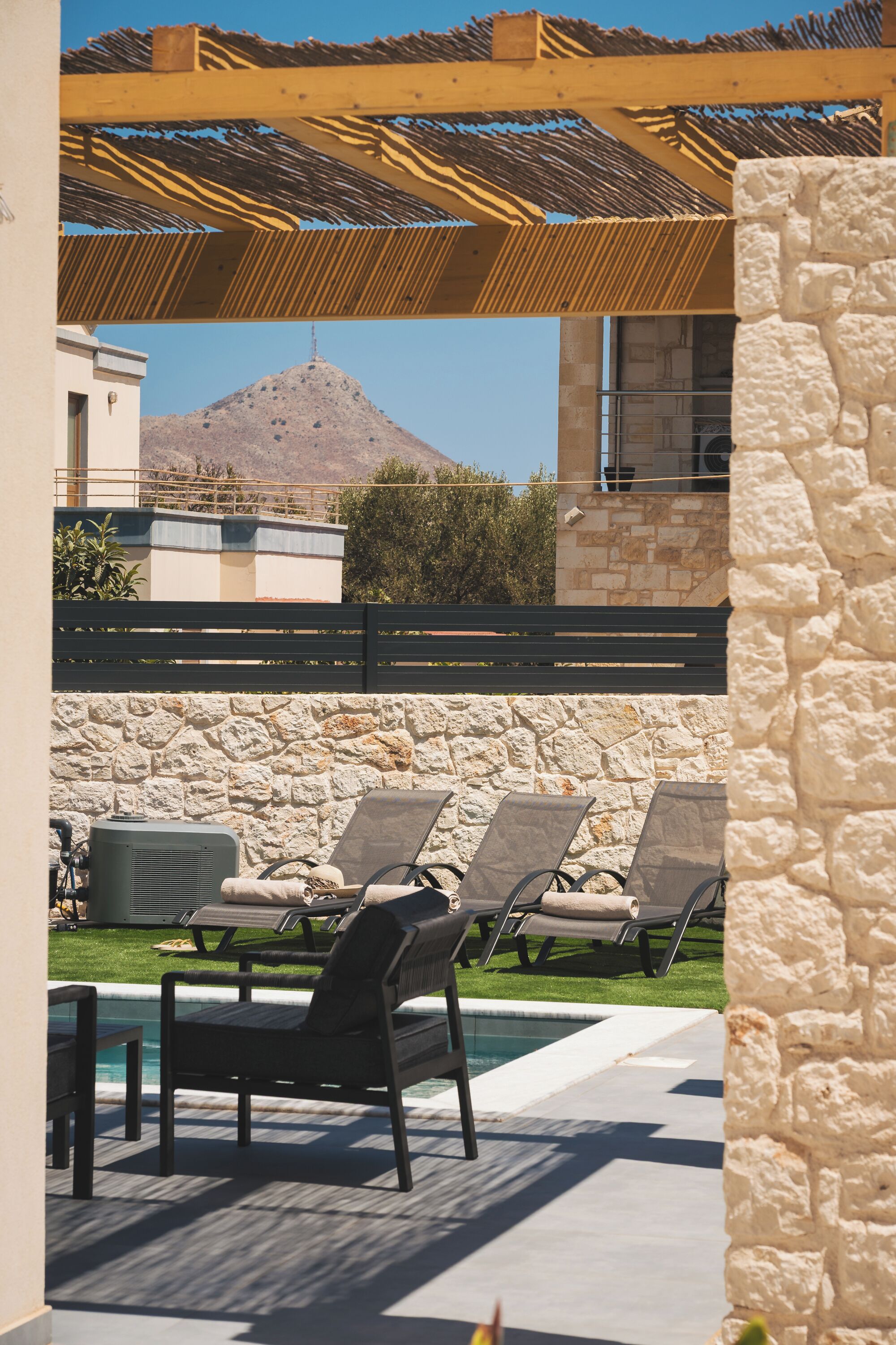 A pool area with lounge chairs, a stone wall, and a mountain view.