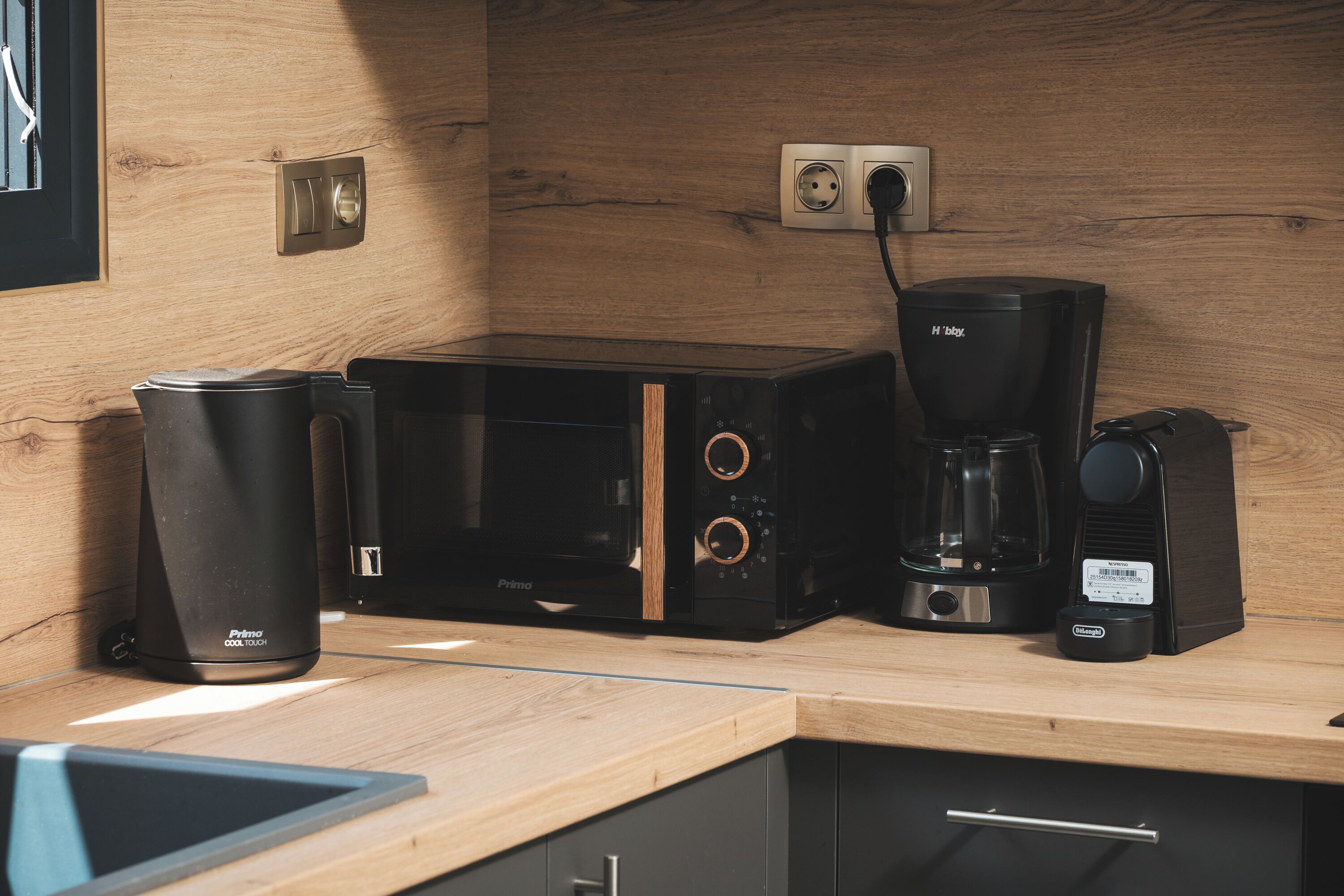 Una cocina con cafetera, tostadora y dispensador de cápsulas de café sobre una encimera de madera.
