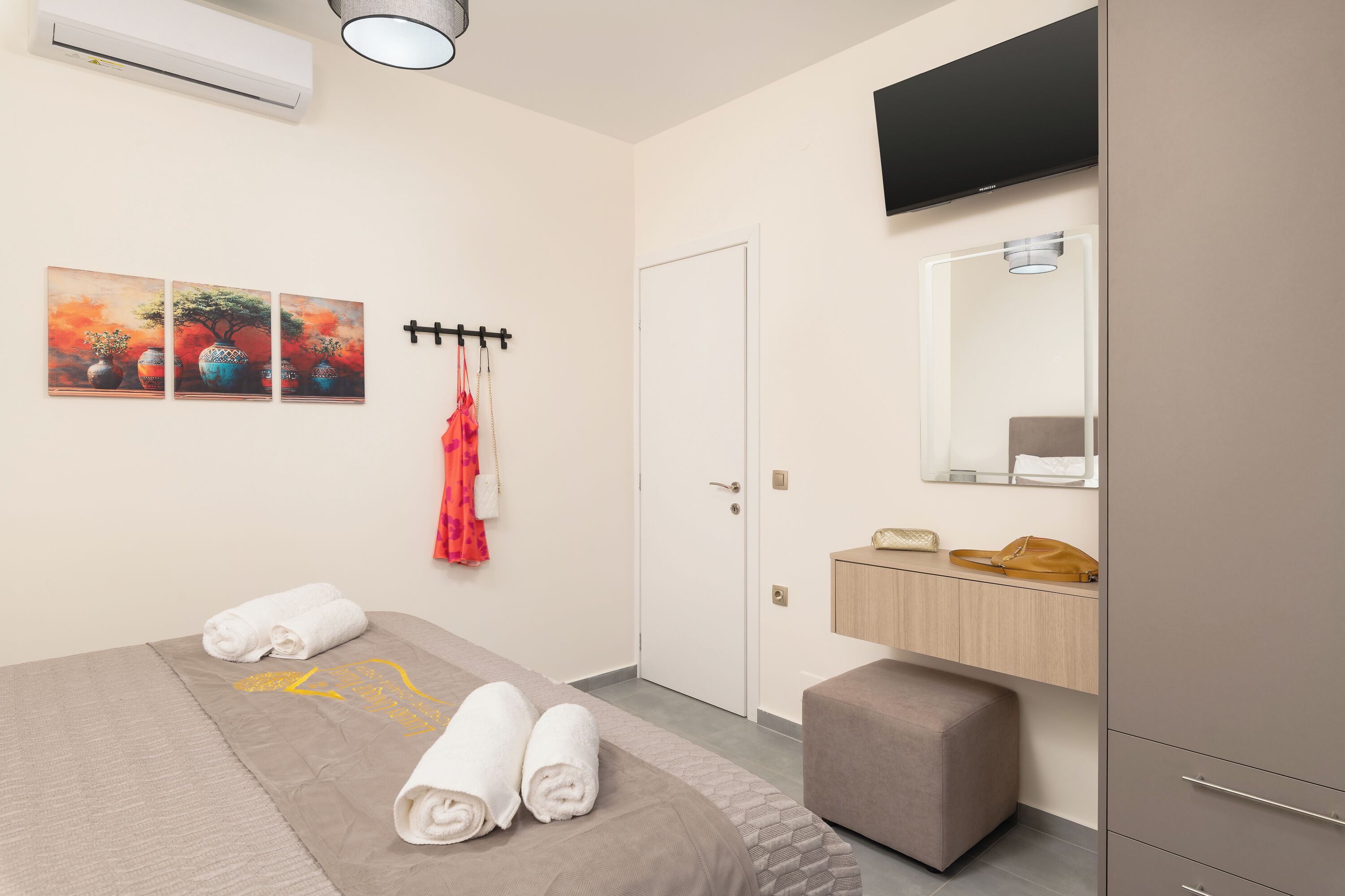 Quarto de hotel com cama, televisão de tela plana presa acima da cômoda, espelho e ar-condicionado fixado na parede.