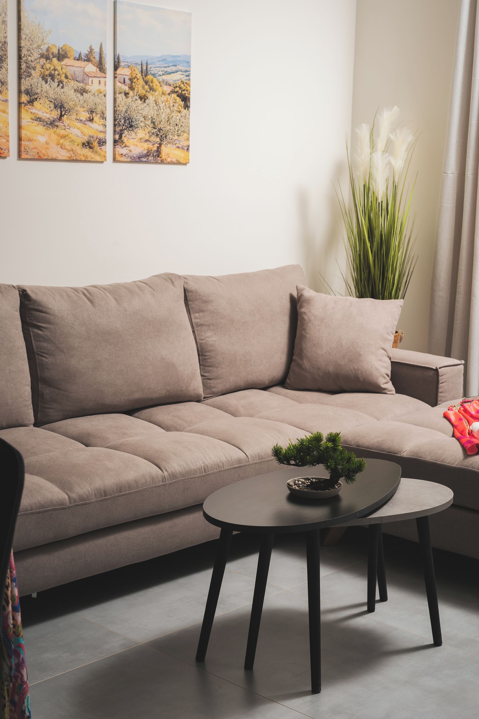 Uma sala de estar moderna com um sofá bege, uma mesa de centro redonda com uma planta e um quadro na parede.