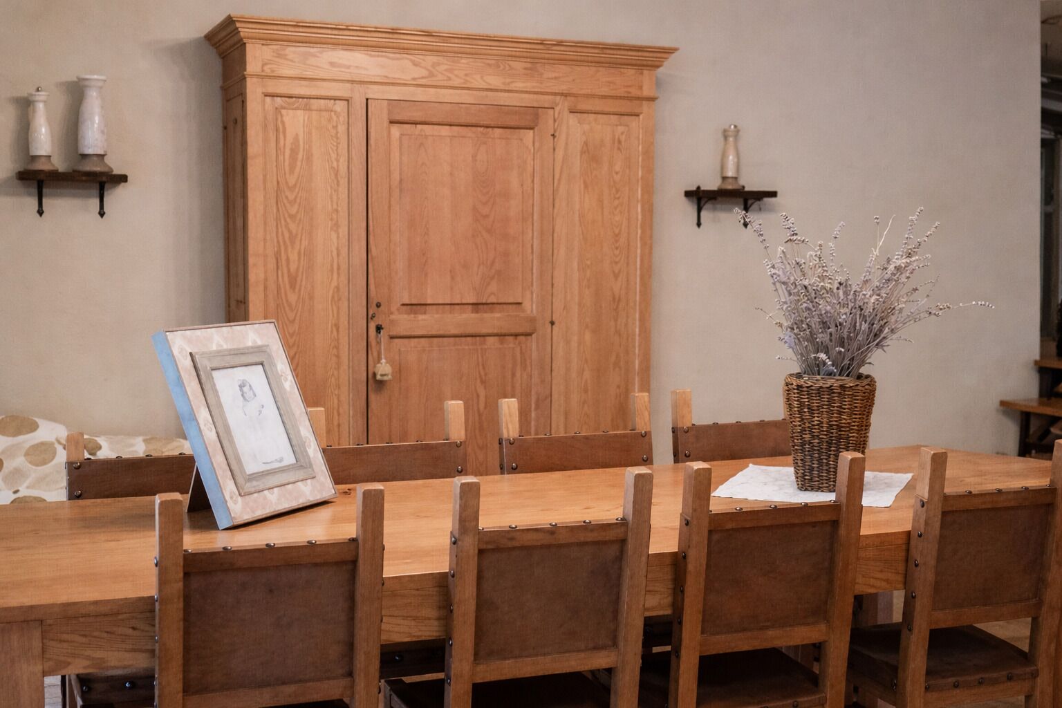 Une table à manger en bois avec six chaises, un grand meuble en bois et deux supports à bougies fixés au mur.