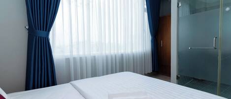 Habitación de hotel con una cama, ropa blanca, una puerta de vidrio y cortinas azules.