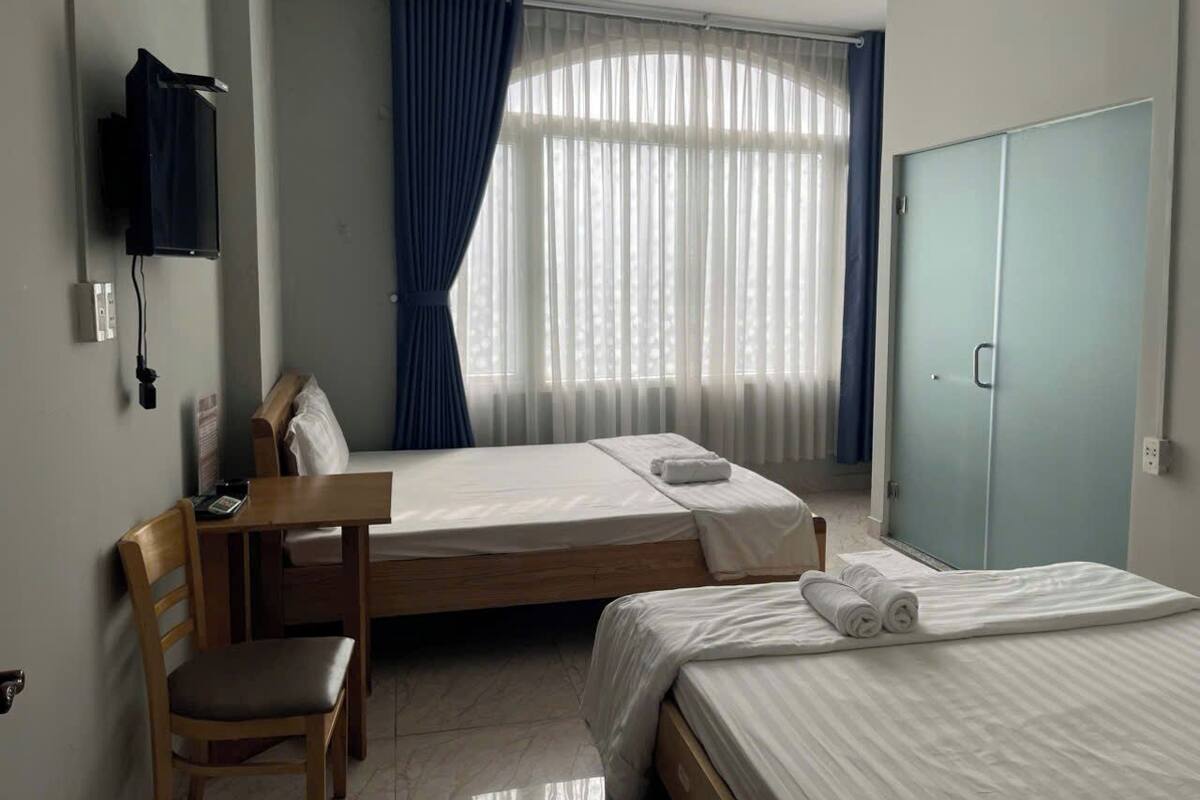 Ein Hotelzimmer mit zwei Betten, einem Holzbstuhl, einem an der Wand befestigten Fernseher und einem Kleiderschrank.
