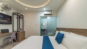 Une chambre d’hôtel comprenant un lit, un bureau avec une chaise, un téléviseur fixé au mur, un appareil de climatisation et une porte de salle de bain.