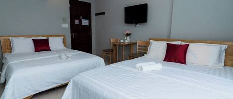 A hotel room with two beds, a small table with chairs, a TV mounted on the wall, and an air conditioning unit.