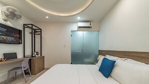 Une chambre d’hôtel équipée d’un lit, d’un bureau avec un ordinateur portable, d’une chaise, d’un ventilateur et d’un appareil de climatisation.