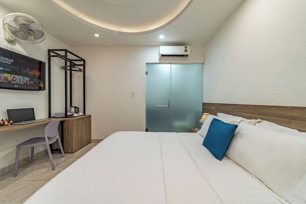 Hotelkamer met een bed, een bureau met een laptop, een stoel, een klemventilator en een airconditioner.