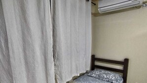 A bedroom with a bed, curtains, an air conditioning unit, and a patterned rug. - Ground floor one-bedroom apartment in a condominium with swimming pools and 100 meters from the sea in Florianópolis, SC. (Florianópolis)