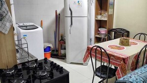 A compact kitchen with a gas stove, a washing machine, a refrigerator, and a dining table with chairs. - Ground floor one-bedroom apartment in a condominium with swimming pools and 100 meters from the sea in Florianópolis, SC. (Florianópolis)