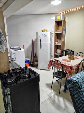 A compact kitchen with a gas stove, a washing machine, a refrigerator, and a dining table with chairs. - Ground floor one-bedroom apartment in a condominium with swimming pools and 100 meters from the sea in Florianópolis, SC. (Florianópolis)
