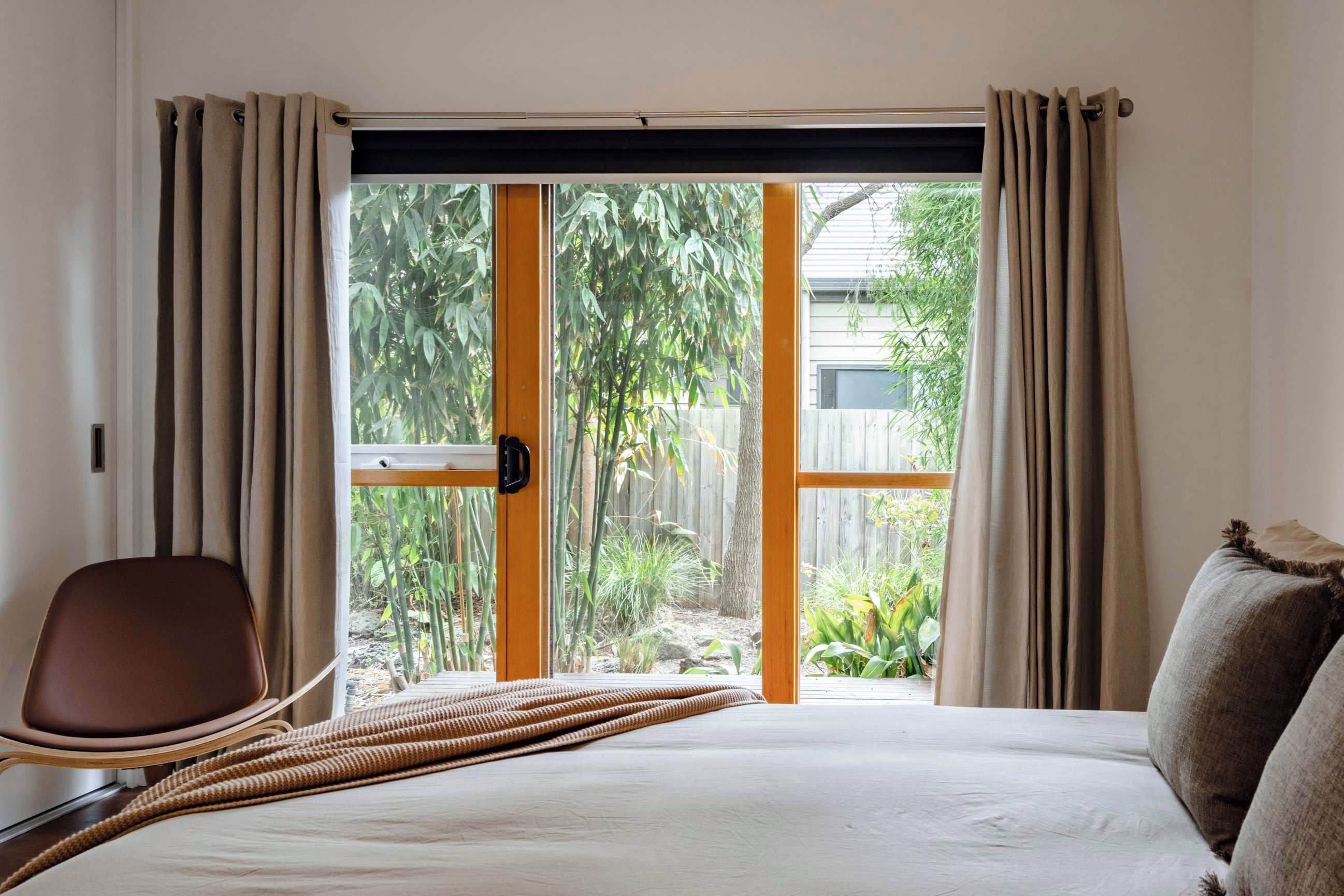 A bedroom with a bed, a chair, and a view of greenery outside.