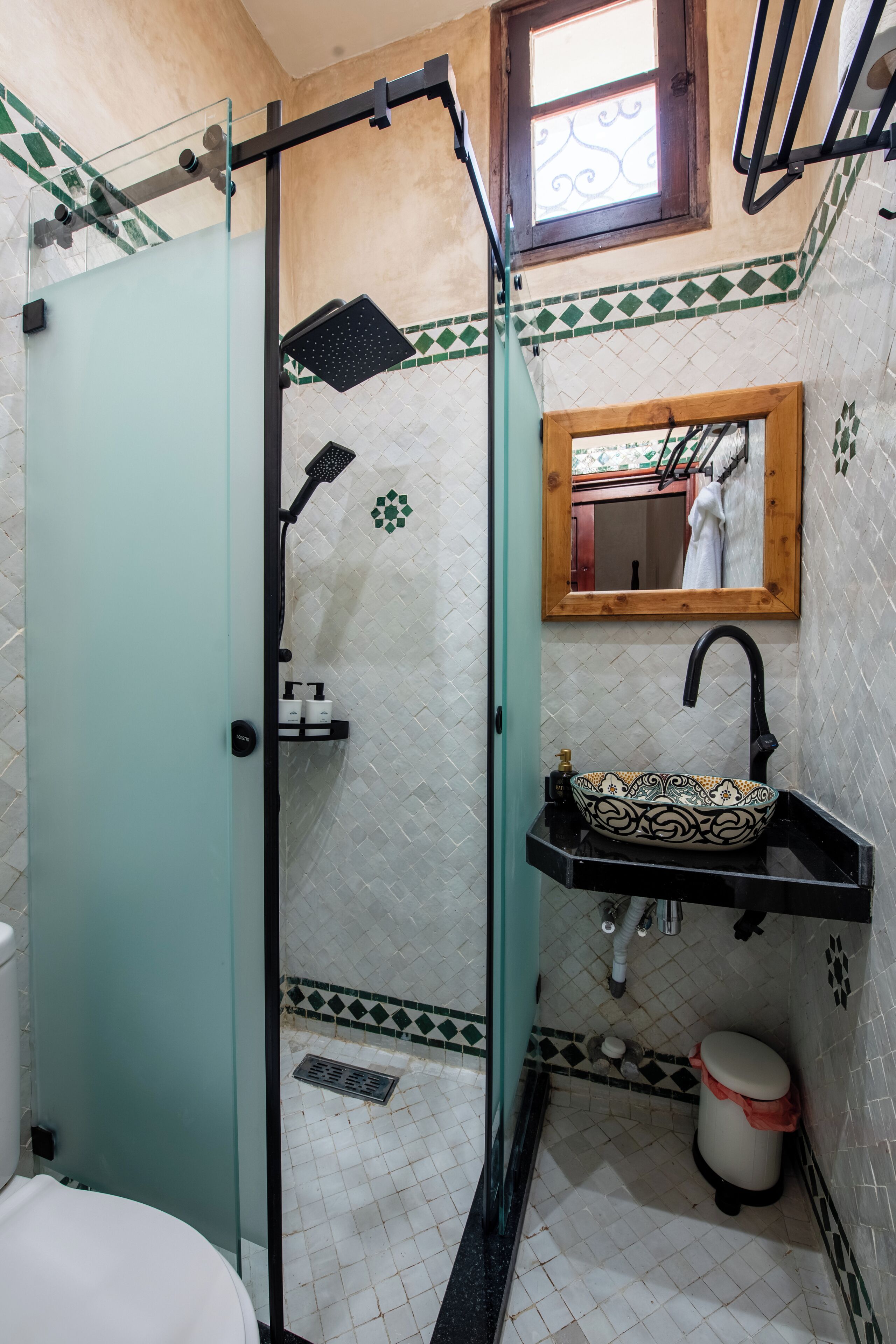 A bathroom with a glass shower enclosure, a sink with a decorative basin, a mirror, and a tiled floor.