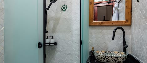 A bathroom with a glass shower enclosure, a sink with a decorative basin, a mirror, and a tiled floor.