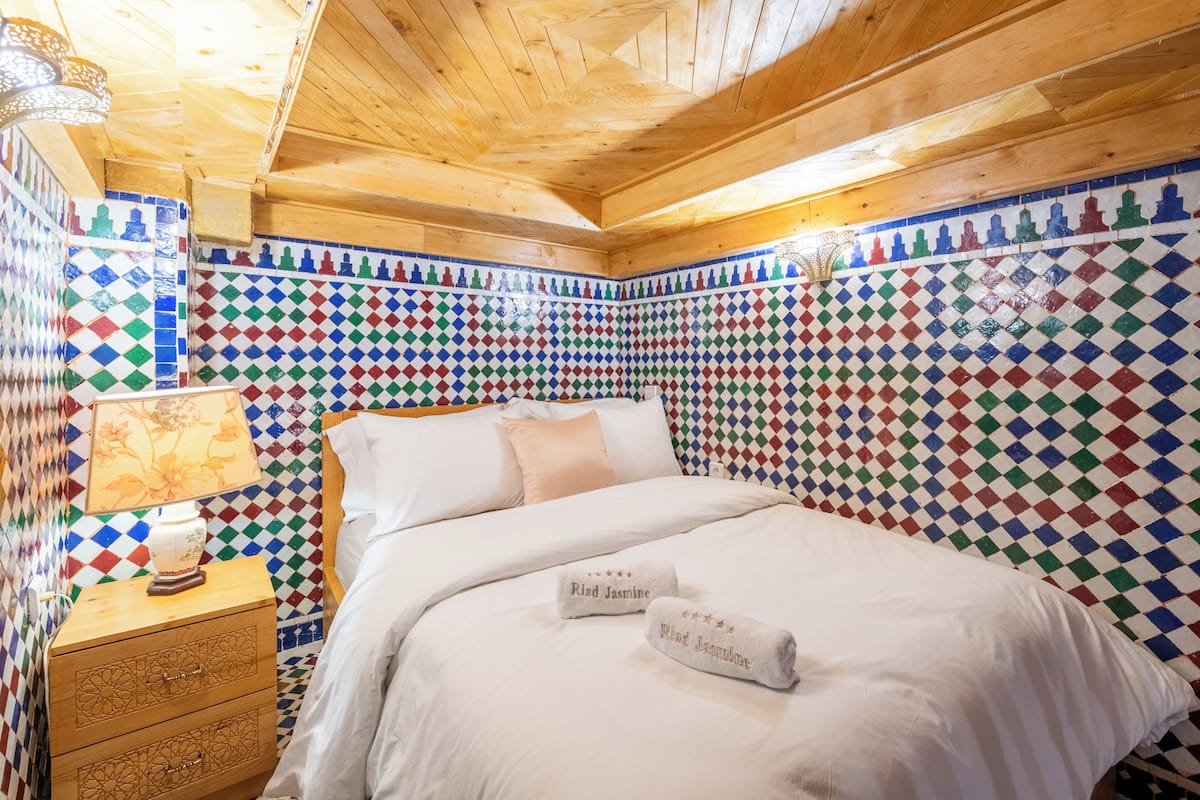 A room with a bed, a nightstand, a lamp, and a colorful mosaic wall.