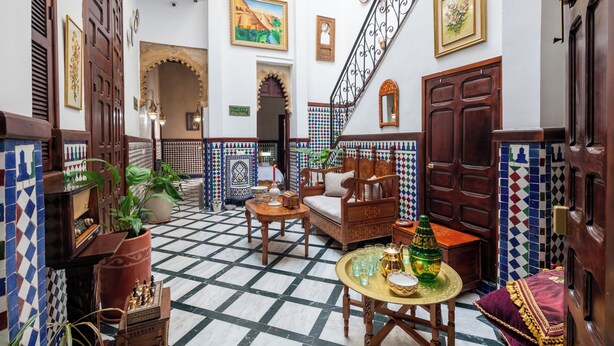 Ein traditionelles marokkanisches Interieur mit Schachbrettfußboden, Holzmöbeln und dekorativen Fliesen.