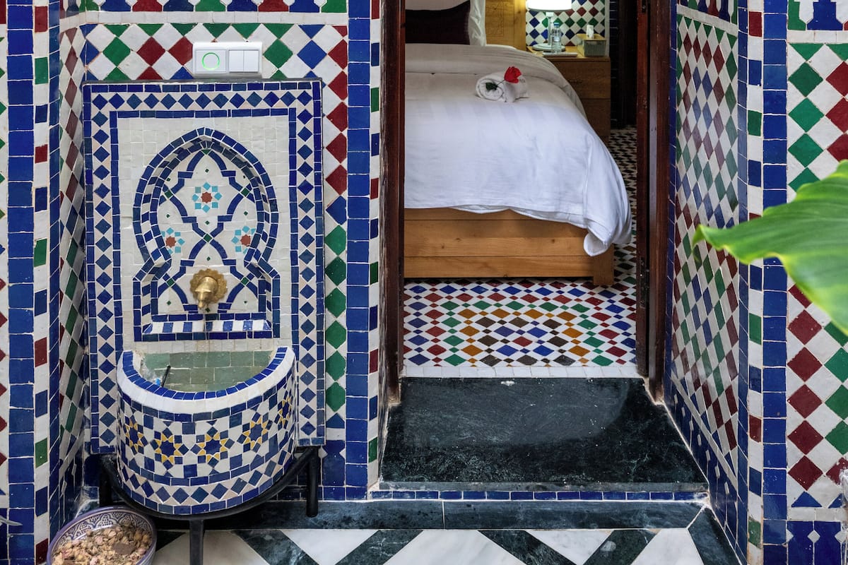 A room with a bed, a small sink, and a tiled wall with a geometric pattern.