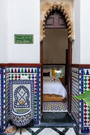 A room with a bed, a small sink, and a tiled wall with a geometric pattern.
