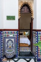 A room with a bed, a small sink, and a tiled wall with a geometric pattern.