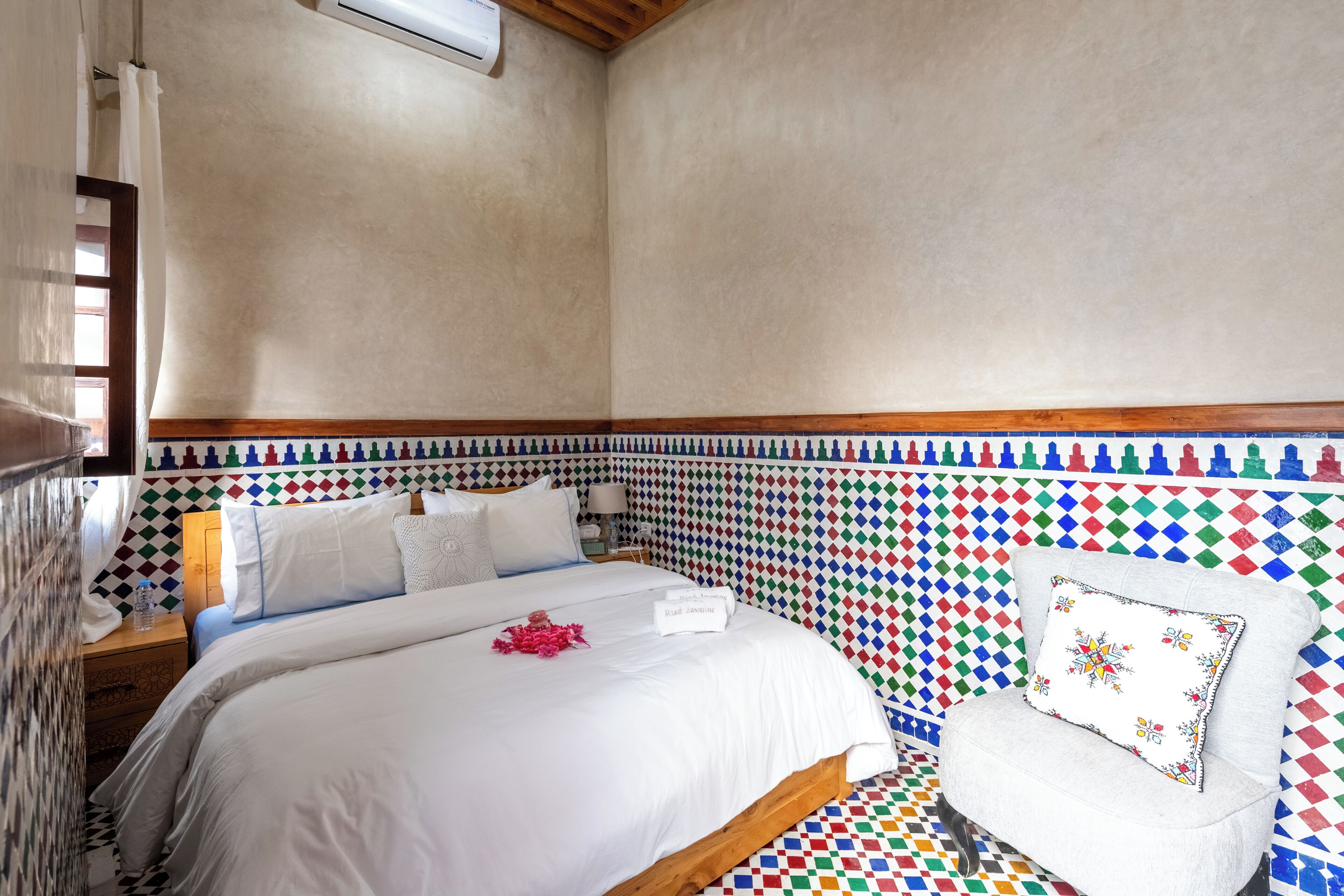 A neatly made bed with white linens, a wooden headboard, and a colorful patterned wall.