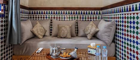 A cozy room with a patterned wall, a beige sofa with decorative pillows, a wooden coffee table with a tray of snacks, and a remote control.