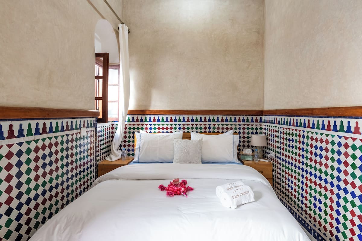 A hotel room with a checkered wall pattern, a bed with white linens, and a nightstand with a lamp.