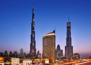 A cityscape with prominent skyscrapers, including a tall, slender tower and a curved building with a golden facade. - Vogue| Fashion Avenue Direct connect to Dubai Mall (Dubai)