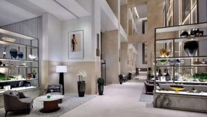 Een moderne hotel lobby met een centrale zithoek, een receptiebalie en een groot raam dat voor natuurlijk licht zorgt.