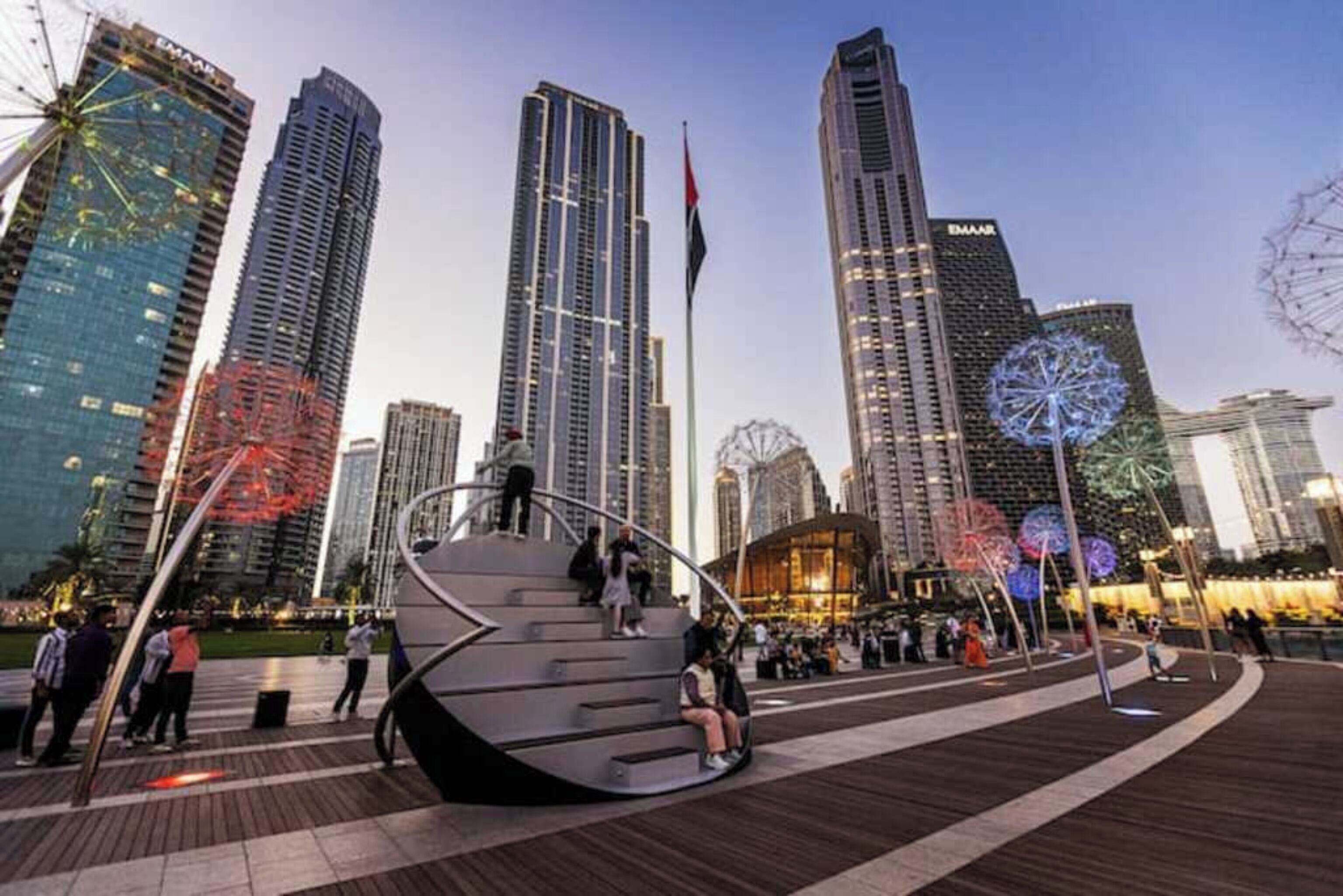 Una plaza urbana moderna con rascacielos, una noria grande y una escultura espiral distintiva.