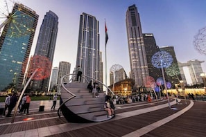 A modern urban plaza with high-rise buildings, a large Ferris wheel, and a unique spiral sculpture. - Vogue| Fashion Avenue Direct connect to Dubai Mall (Dubai)