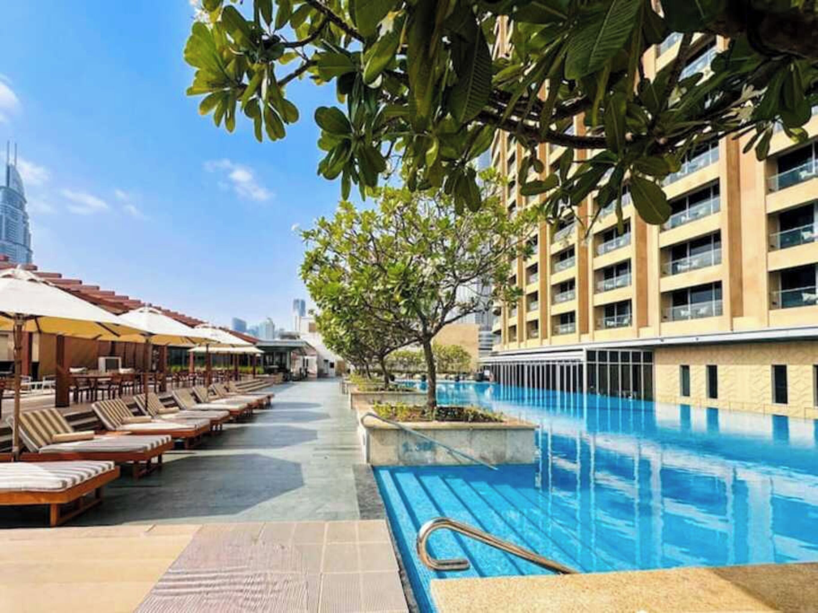 Ein Poolbereich mit Liegestühlen und Sonnenschirmen, ein Schwimmbecken und ein Gebäude mit mehreren Balkonen.