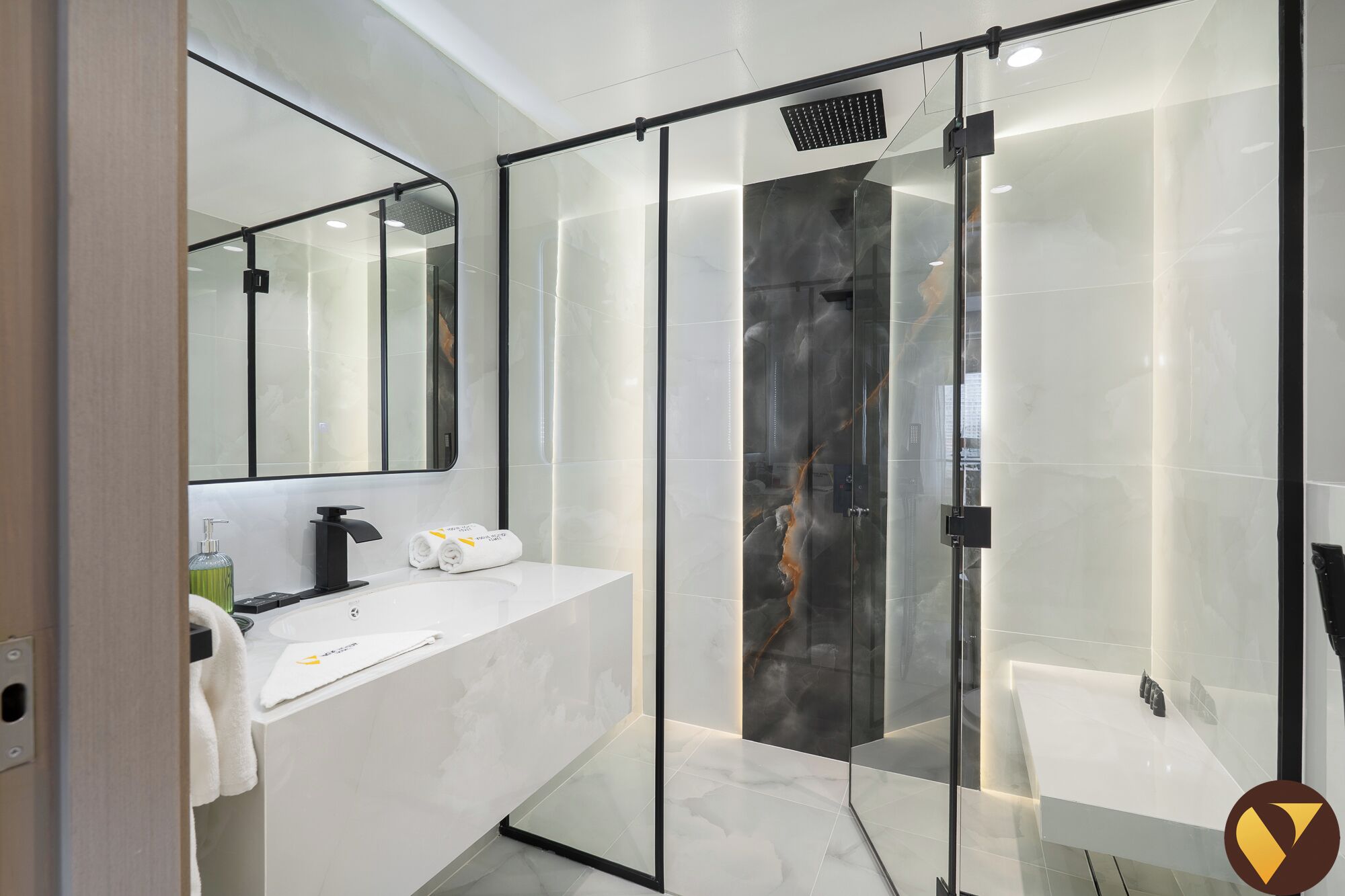 A modern bathroom with a glass-enclosed shower, a white vanity with a mirror, and a marble-tiled wall.