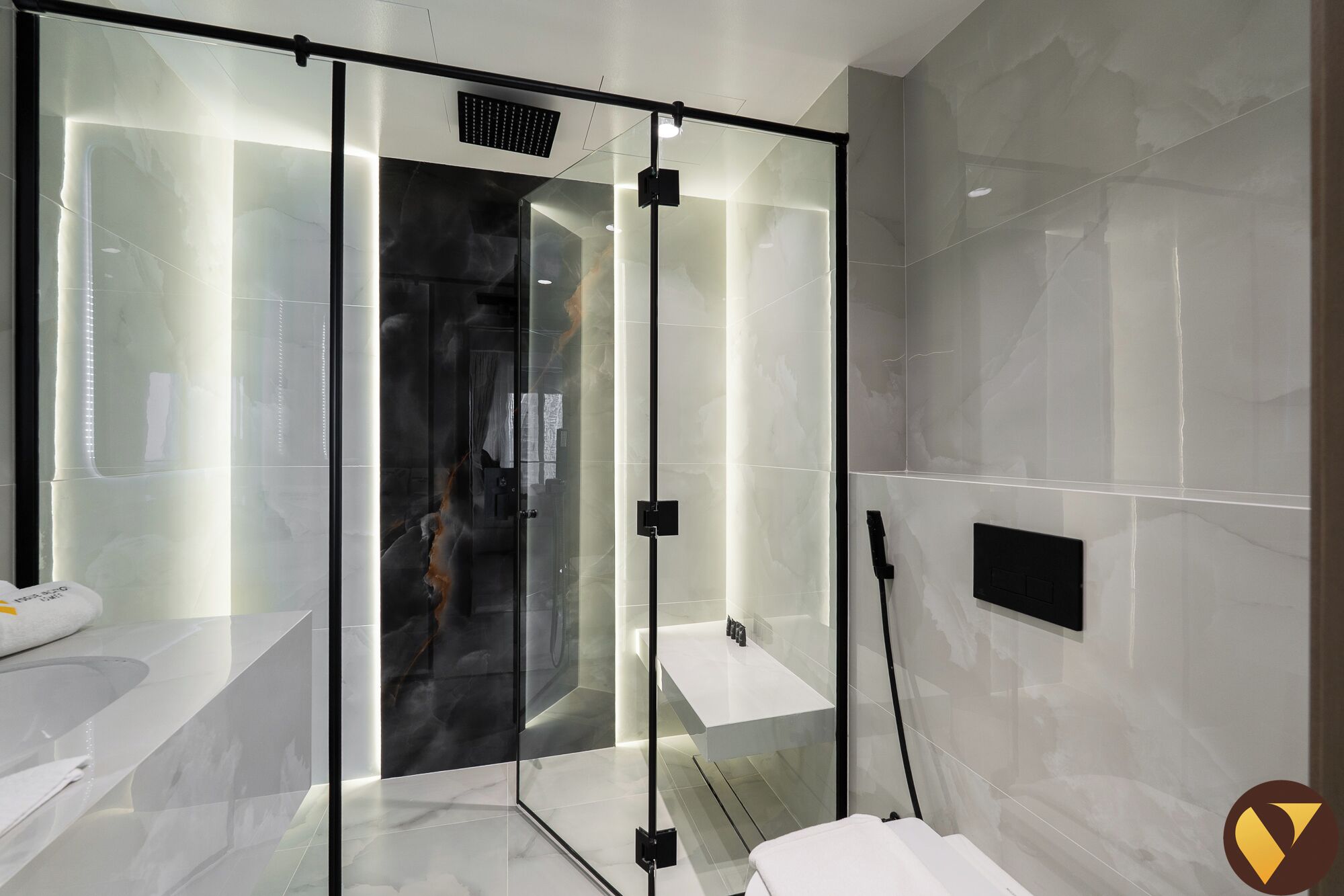 Un baño moderno con cabina de ducha de vidrio, un lavabo blanco y una pared de mármol.