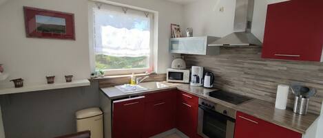 A compact kitchen with red cabinets, a microwave, a coffee maker, and a window with a view of greenery.