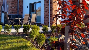 A modern two-story house with a brick facade, a flat roof, and a small front porch with outdoor seating.