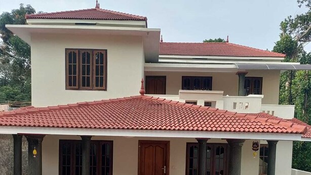 Une maison à deux étages, avec un toit recouvert de tuiles rouges, un porche et un chemin d’accès aux motifs rouges et noirs.